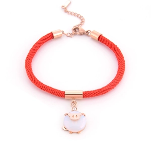 Close-up of red woven bracelet with rose gold pig charm and opal inlay detail