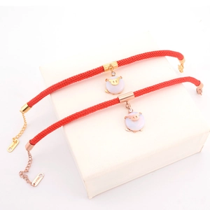 Detail of red braided rope bracelet with golden pig charm and S-STEEL clasp on jewelry box
