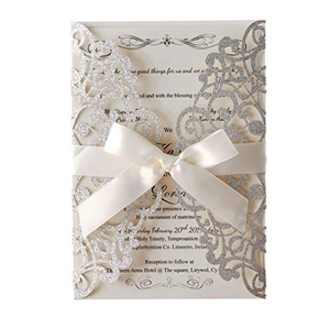 Detail of silver glitter laser-cut wedding invitation with cream card and white satin bow