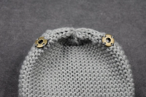 Detailed close-up of grey cable knit texture with vintage copper metal snap buttons