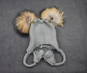 Close-up of grey cable-knit baby trapper hat with two fluffy faux fur pom poms