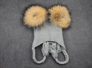 Detail of gray knit baby hat with dual faux fur pom-poms and braided ear flaps