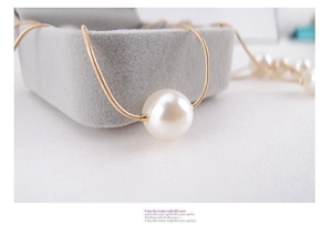 Close-up of a large white round pearl pendant on a thin gold snake chain necklace