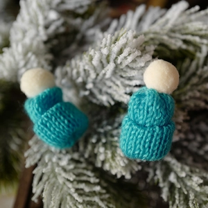Miniature teal blue knitted Christmas hats with white pom-poms on frosted pine branches