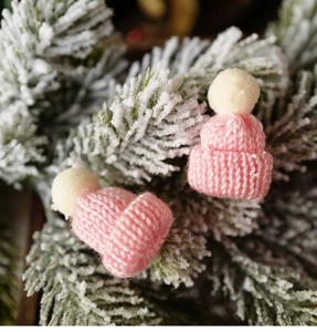 Close-up of pink knitted mini Christmas hats with white pom-poms on snowy pine branches