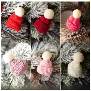 Detailed view of six colorful mini knitted Christmas hats with pom-poms on pine branches