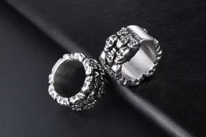 Close-up of dual stainless steel rings featuring intricate 3D skull relief patterns