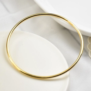 Close-up of a 2mm gold-plated titanium steel minimalist bangle on a white ceramic plate