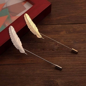 Detailed view of silver and gold feather lapel pins with safety caps on a dark wood background