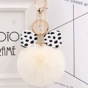 Close-up of beige plush pompom keychain with polka dot bow and crystal details
