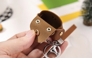 Handheld view of a brown leather mini pouch with a silver keychain ring and snap button