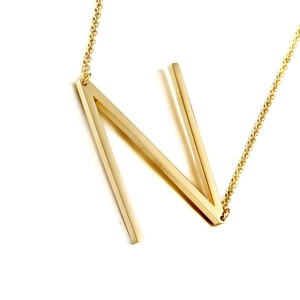 Close-up of a minimalist gold initial N pendant with a brushed metal texture on a thin chain