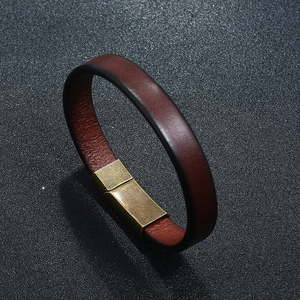 Detail of dark brown leather bracelet with vintage brass magnetic buckle on black background