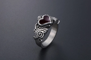 Detail of silver steel ring with red heart gemstone and intricate scroll patterns