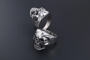 Close-up of two stackable stainless steel skull rings for men with a polished silver finish