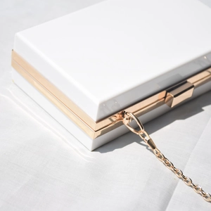 Detail view of white acrylic clutch bag with gold metal frame and chain strap