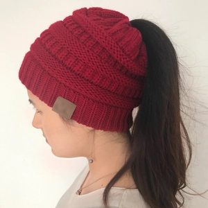 Close-up of red cable knit ponytail beanie featuring a functional top opening and leather patch