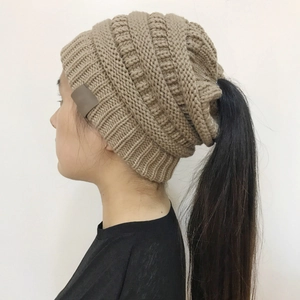 Detail of brown cable knit ponytail beanie with top hole and decorative side leather patch
