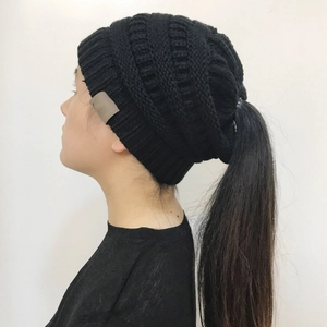 Side view of a black knit ponytail beanie with a chunky texture on a model