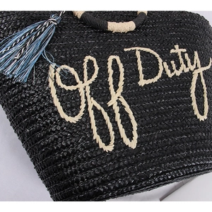 Detail of woven straw tote bag with Off Duty embroidery and blue fringed tassel charm