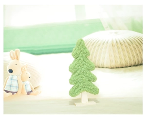 Close-up of a green knitted wool Christmas tree ornament with a natural wooden base