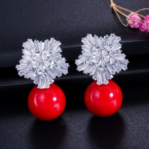 Detail of flower shaped earrings with white zircon stones and a large red pearl drop