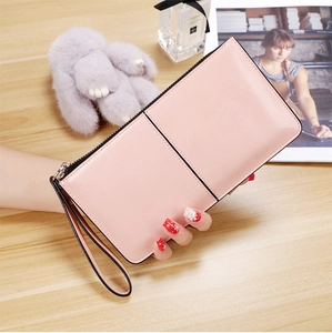 Pink long leather wallet held by hand against a stylish wooden table background