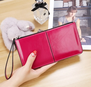 Long rose red oil wax leather wallet held in hand featuring zipper and wrist strap detail