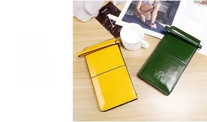 Long leather clutch wallets in yellow and green with wrist straps on wooden table