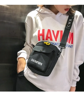 Detail of black canvas crossbody bag with yellow zipper pull and lettered strap on model