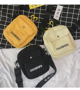 Detailed stack of yellow, white, and black canvas crossbody bags with adjustable straps