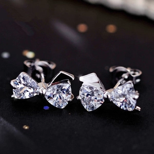 Close-up of silver bowknot stud earrings with sparkling cubic zirconia on a dark starry background