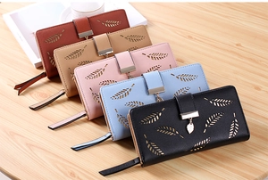 Flat lay of five long leaf wallets in various colors on a light wood background