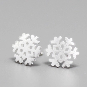 Macro detail of snowflake-shaped matte silver stud earrings with brushed metal texture