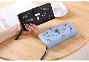 Detailed view of women's long zip-around leaf pattern wallet with tassel on wooden desk