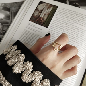 Dettaglio di un anello a stella dorato indossato al dito su sfondo di una rivista d'arte