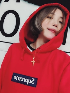 Detail of a golden angel wing pendant necklace worn over a red streetwear hoodie