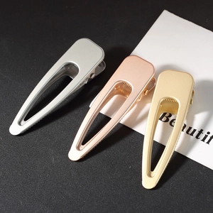 Three minimalist metal hair clips in silver, pink, and gold displayed on a dark surface
