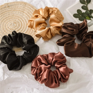 Flat lay of four satin hair scrunchies in black, gold, brown, and caramel colors