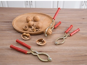 Close-up of red handle nutcracker with metal jaws and walnuts on a wooden plate