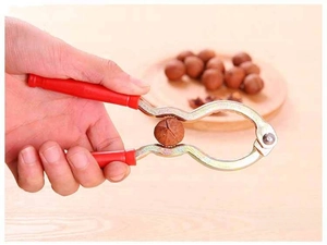 Macro detail of red handle nutcracker tool crushing a small walnut on a wooden desk