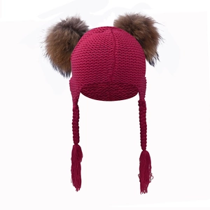 Detail of dark red knit baby hat with earflaps, long braids, and twin brown pom-poms