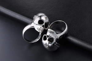 Macro shot of two silver stainless steel skull rings on black textured leather surface