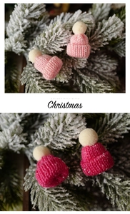 Close-up of pink and rose mini knit Christmas hats on cedar branches for DIY garland