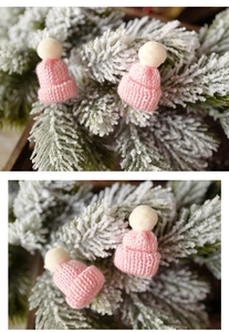 Close-up of pink mini knitted Christmas hats with white pom-poms on pine branches