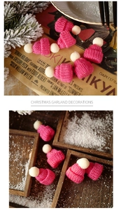 Mini pink knitted Christmas hats with white pom-poms on vintage newspaper and pine branches