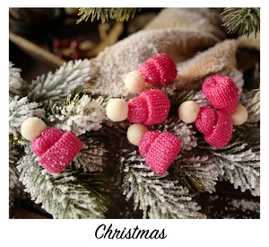 Pink knit mini Christmas hats with white pom-poms on snowy pine branches detail