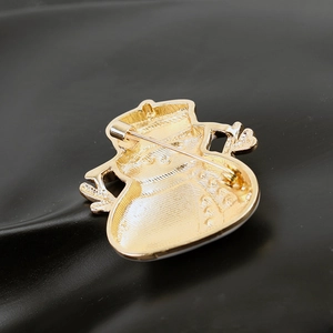 Detailed back view of golden snowman brooch featuring a metal pin clasp on black wavy surface