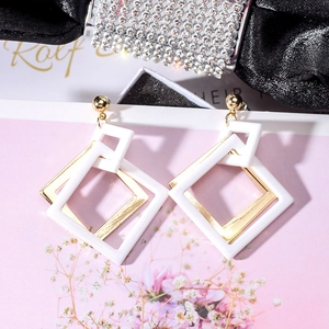 Close-up of geometric white acrylic and gold metal square earrings on a floral card