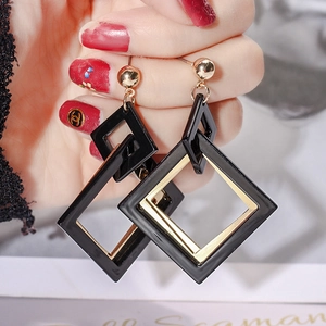 Macro shot of geometric black lacquer and gold double diamond earrings held by hand